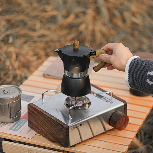 Person using a portable coffee maker on a wooden table outdoors