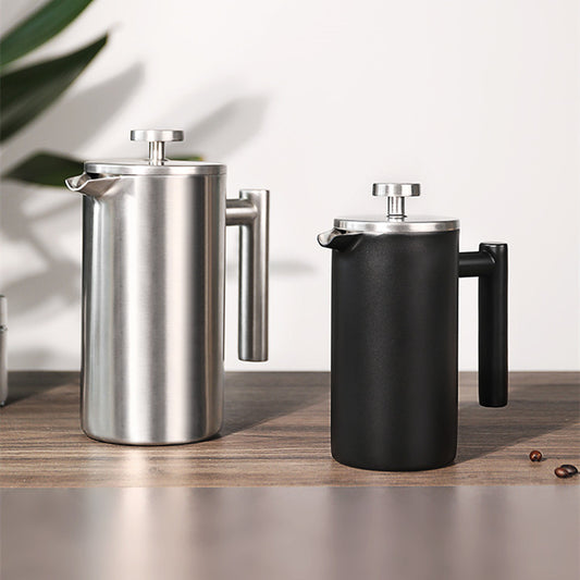 Two French presses, one silver and one black, on a wooden surface with a light background.