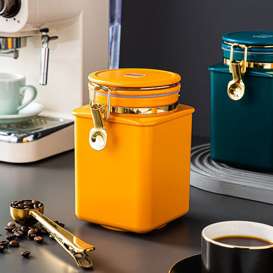 Orange kitchen canister with gold clasp on a kitchen counter with coffee beans and a cup.