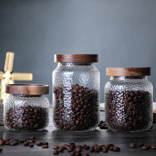 Set of three Scandinavian-style glass coffee storage jars with airtight acacia wood lids for coffee beans.