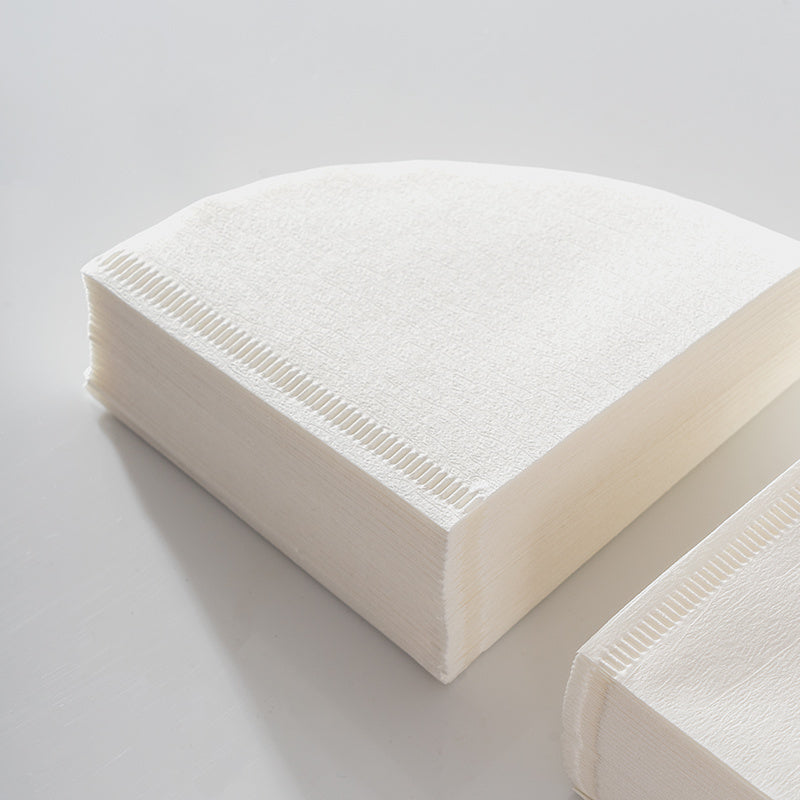 Stack of V-shaped coffee filter papers, highlighting the quality and texture of the raw wood pulp material. Shop now