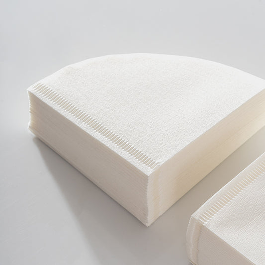 Stack of V-shaped coffee filter papers, highlighting the quality and texture of the raw wood pulp material. Shop now