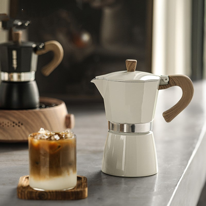 White espresso pot with wooden handle and lid on a kitchen counter with a glass of iced coffee.