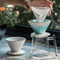 A Muvna Hoshikawa ceramic pour-over coffee dripper set in Hoshikawa White, featuring a dripper on a glass carafe, with another dripper on the side. The image highlights the elegant design and minimalist style. Shop NOW
