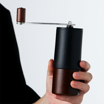 Person holding compact black and wood manual coffee grinder. Ideal for home coffee lovers.