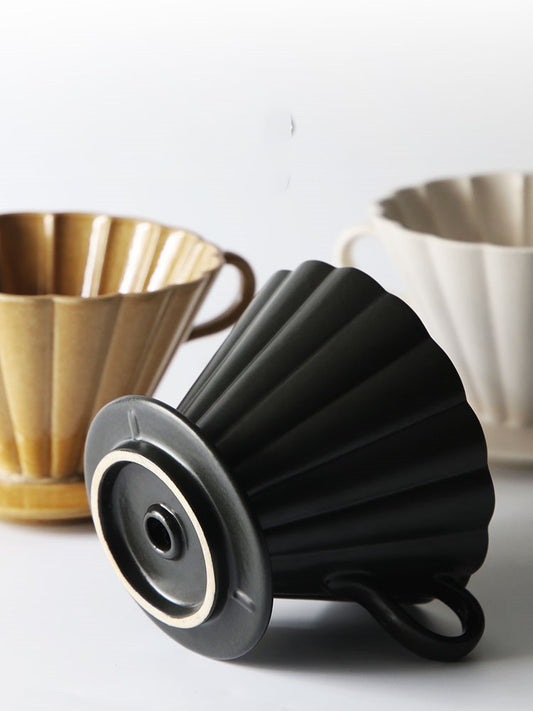 Black silicone coffee filter on a white surface with wooden and ceramic coffee filters in the background. SHOP NOW