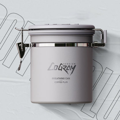 A grey Coffee Plus Breathing Canister, open with a 7g coffee scoop resting on a pile of fresh coffee beans. Another canister is visible in the background. Shop NOW