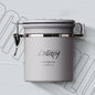 A grey Coffee Plus Breathing Canister, open with a 7g coffee scoop resting on a pile of fresh coffee beans. Another canister is visible in the background. Shop NOW