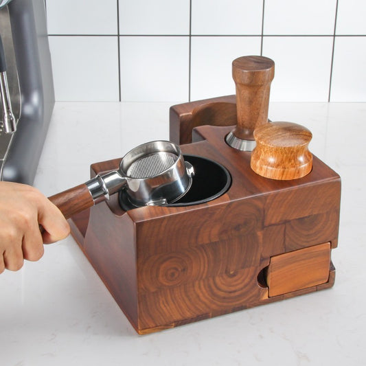 Person placing a portafilter into the built-in knock box of a dark wooden espresso tool organizer.