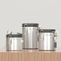 A set of three silver airtight coffee canisters with a matching stainless steel scoop on a wooden table. The canisters feature a modern design with a latch and a date tracker on the lid. Perfect for keeping coffee beans fresh." Shop now!
