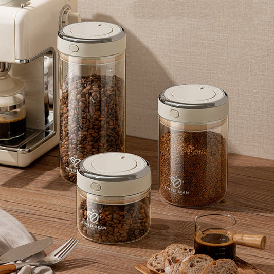 Trio of modern glass coffee storage canisters in various sizes, with warm gray lids, filled with coffee beans and ground coffee on a kitchen counter. BUY NOW