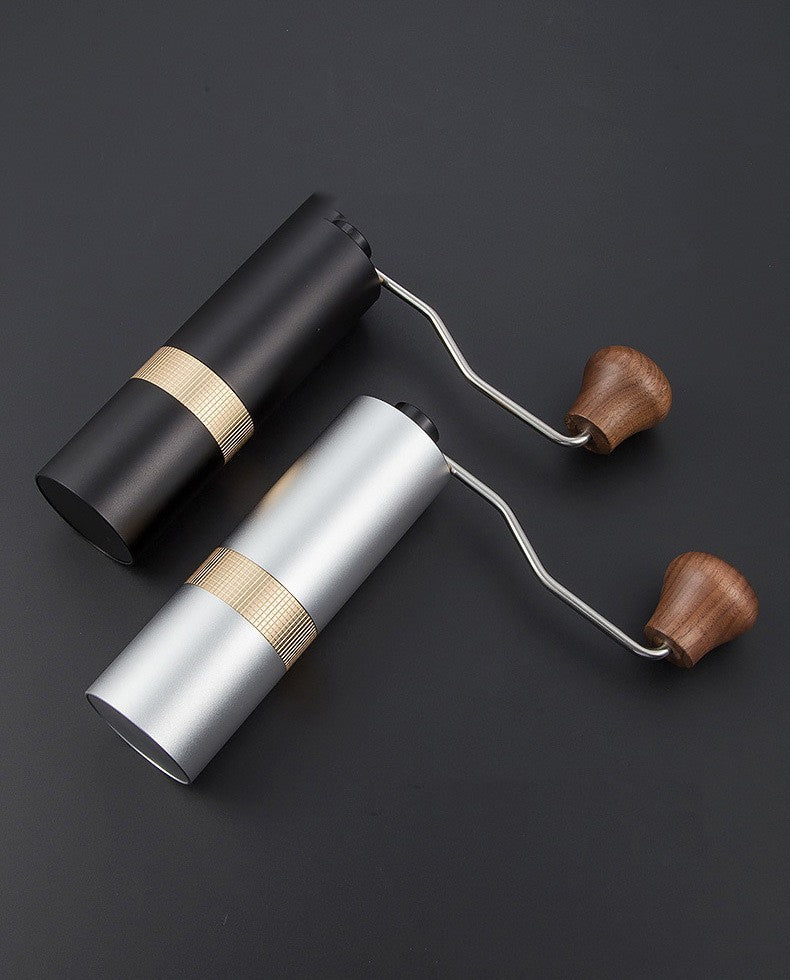 Two portable manual coffee grinders, one in matte black and one in silver, with golden accents and wooden handles. Perfect for coffee enthusiasts.