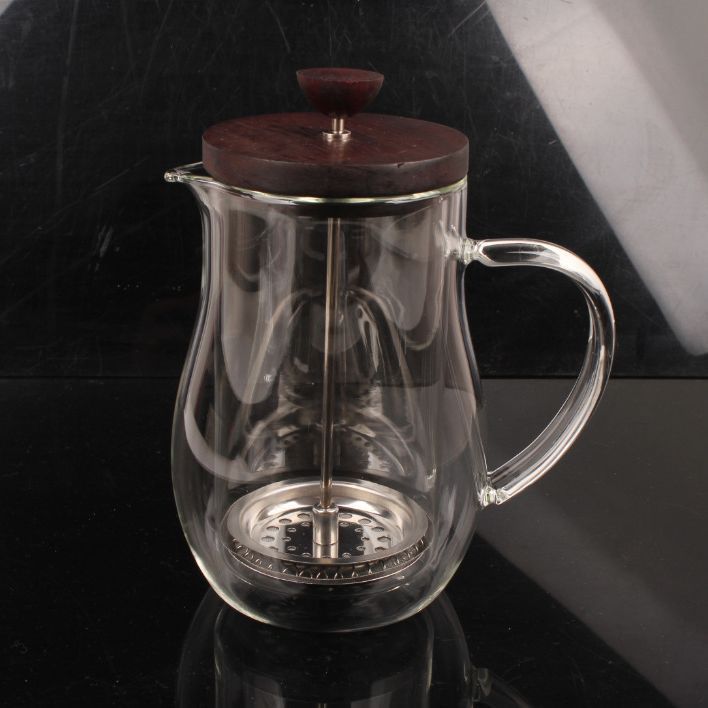 Clear glass teapot with wooden lid on a reflective black surface