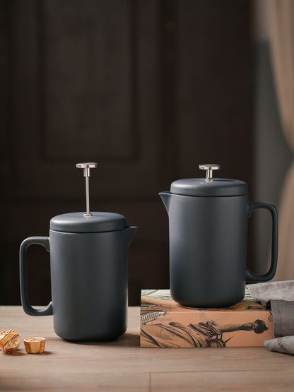 Two black ceramic coffee presses on a wooden surface with a dark background