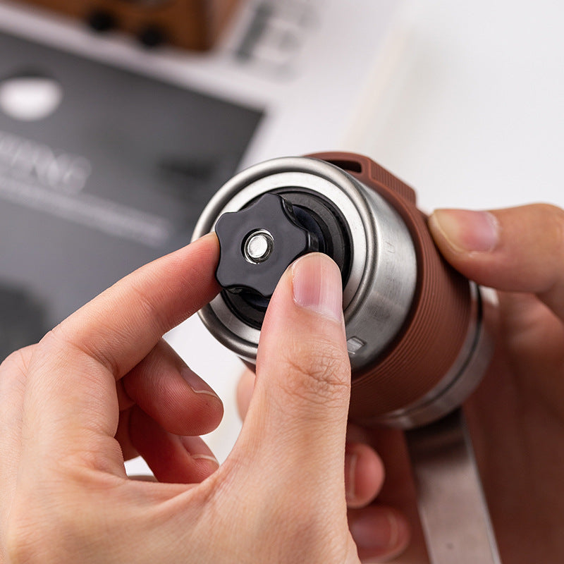 Hands adjusting grind setting on manual coffee grinder. Black ceramic burr for precise, custom coffee grounds.