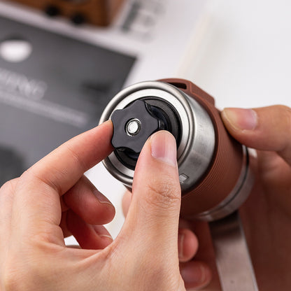 Hands adjusting grind setting on manual coffee grinder. Black ceramic burr for precise, custom coffee grounds.