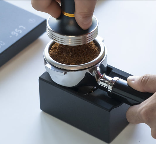Hand using a coffee tamp to compress ground coffee in a portafilter. Buy now