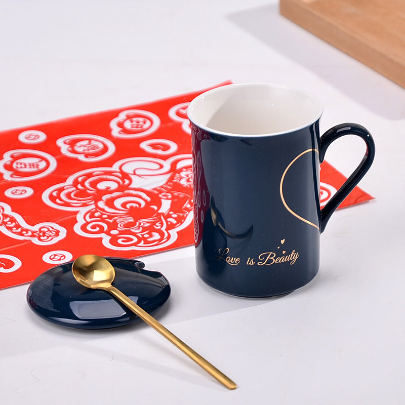 Navy blue mug with 'Love is Beauty' text, gold spoon, and red patterned mat on white surface