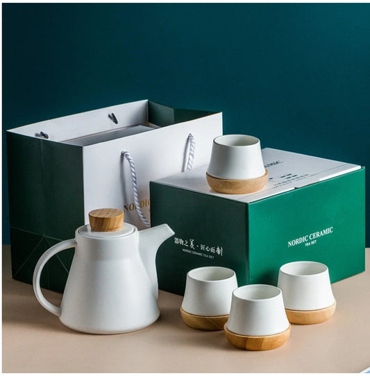 Nordic ceramic tea set with teapot and cups on a beige surface against a teal background.