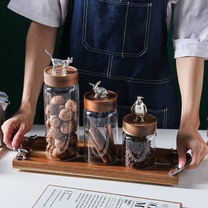 Person holding a tray with glass jars featuring animal-shaped lids on a table.