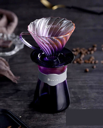 Purple and pink glass coffee dripper on a dark surface with coffee beans.