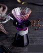 Purple and pink glass coffee dripper on a dark surface with coffee beans.