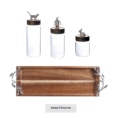 Set of four glass containers with animal figurines on lids and a wooden tray with leaf handles on a white background.