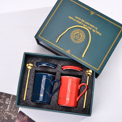 Set of two mugs and two spoons in a decorative box with text on a white background