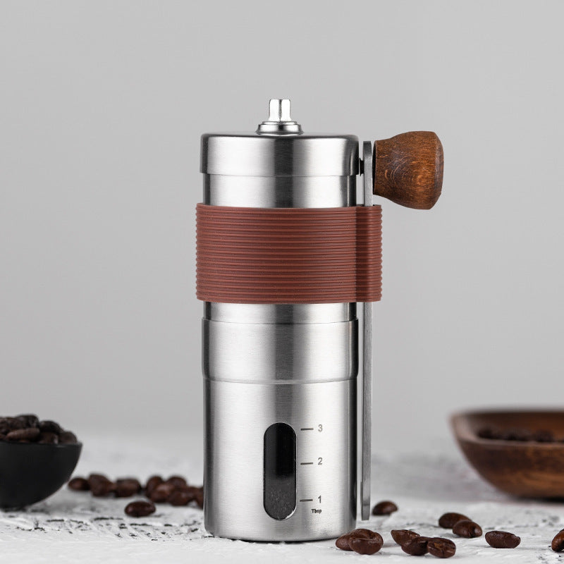 Stainless steel manual coffee grinder on counter with coffee beans, highlighting its modern design for home baristas.