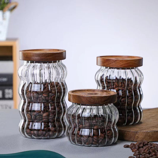 Three glass jars with wooden lids containing coffee beans on a light surface. 
SHOP NOW!