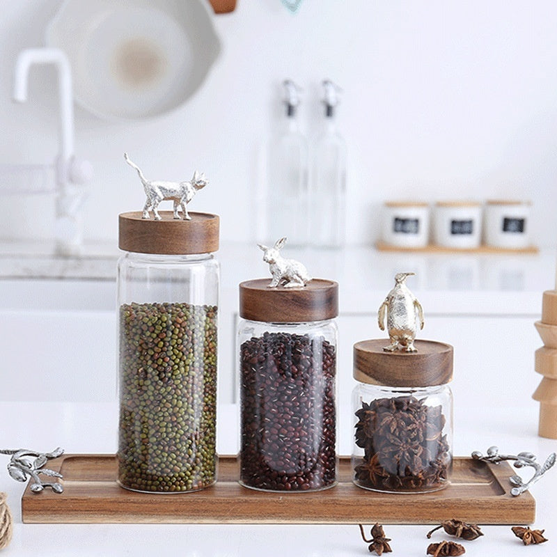 Three glass jars with wooden lids on a wooden tray in a kitchen setting.
