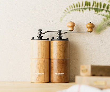 CAFÉDE KONA manual coffee grinders light and dark wood side by side on table, home coffee brewing.
