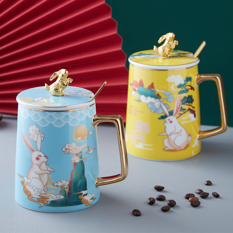 Two ceramic mugs with rabbit designs on a gray surface with coffee beans.