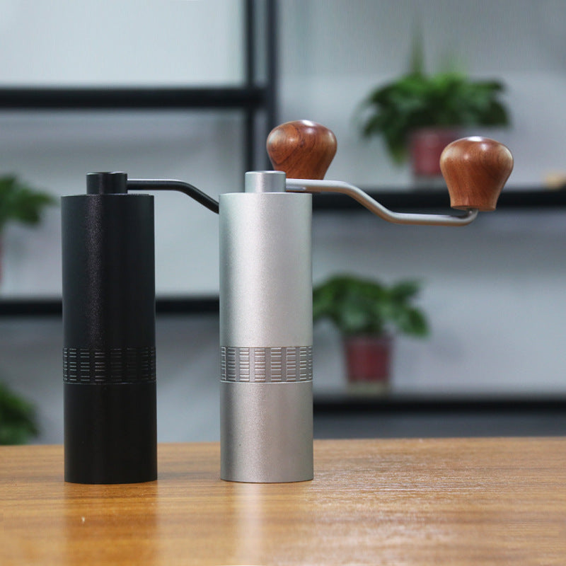 Two manual coffee grinders, one black and one silver with wooden handles, on a wooden surface.
