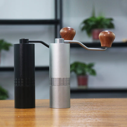 Two manual coffee grinders, one black and one silver with wooden handles, on a wooden surface.