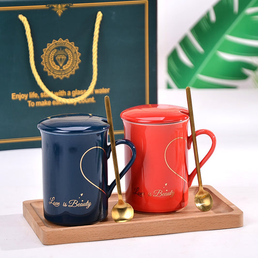Two mugs, one blue and one red, with spoons on a wooden tray, in front of a branded gift bag.