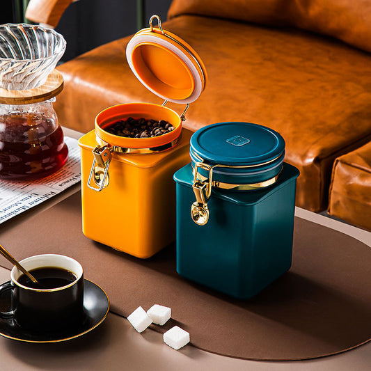 Two small containers, one orange and one blue, on a table with coffee and sugar.