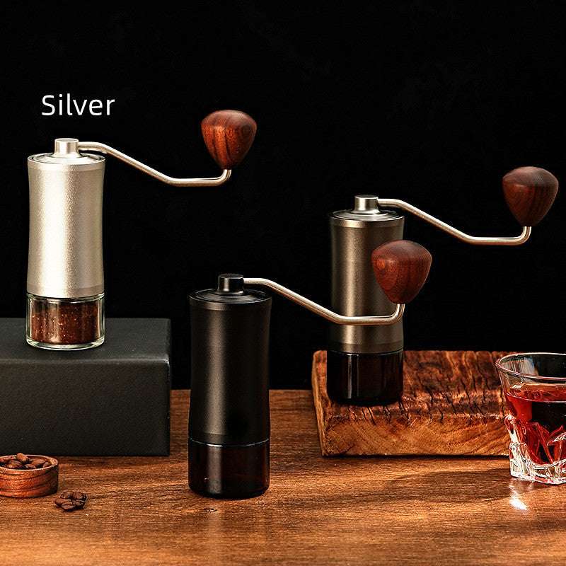 Three manual coffee grinders in different colors on a wooden surface with a dark background.