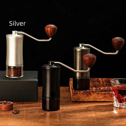 Three manual coffee grinders in different colors on a wooden surface with a dark background.