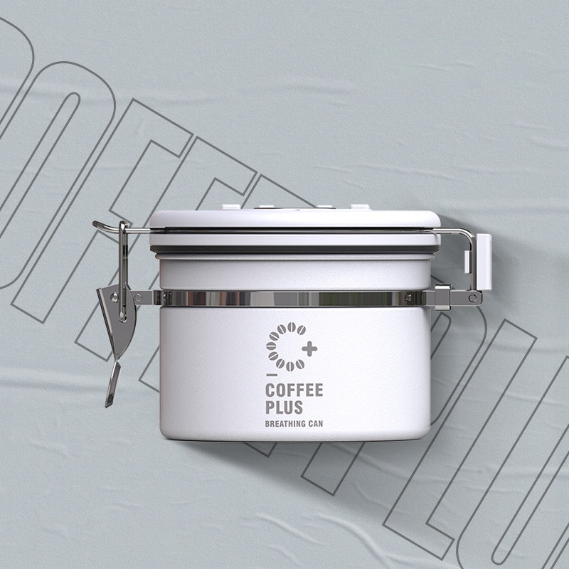  Close-up of a white Coffee Plus Breathing Canister, open to show dark roasted coffee beans inside. A one-way valve on the lid helps keep beans fresh.