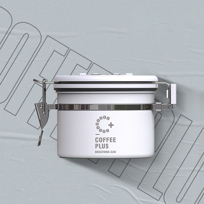 Close-up of a white Coffee Plus Breathing Canister, open to show dark roasted coffee beans inside. A one-way valve on the lid helps keep beans fresh.