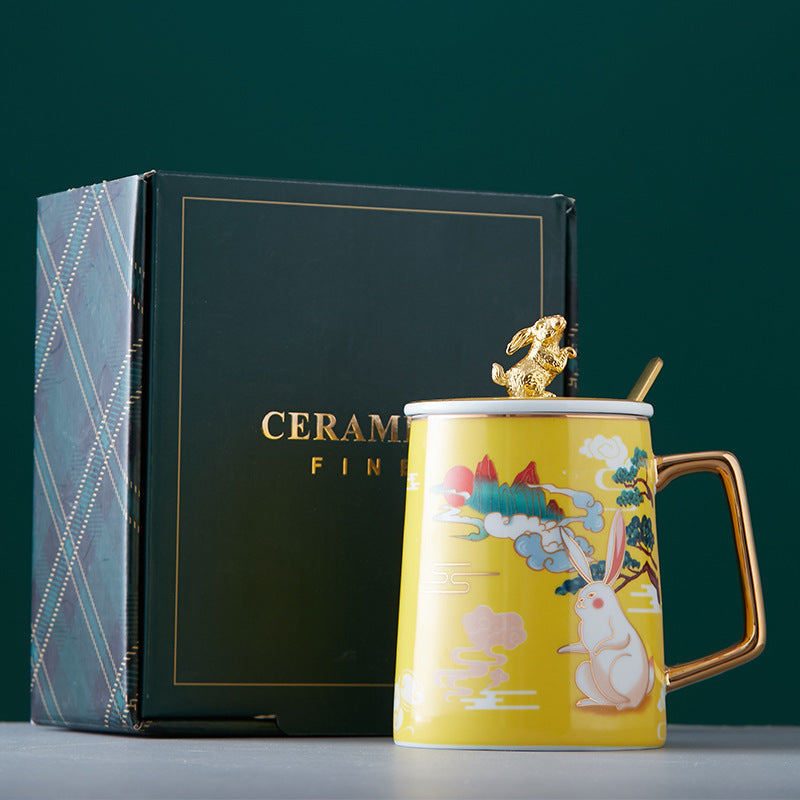 Yellow ceramic mug with decorative elements and a gold handle, next to a black gift box with 'Ceramic Fine' branding.