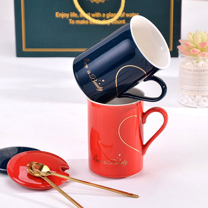 Two mugs, one red and one blue, with a heart design on a white surface.