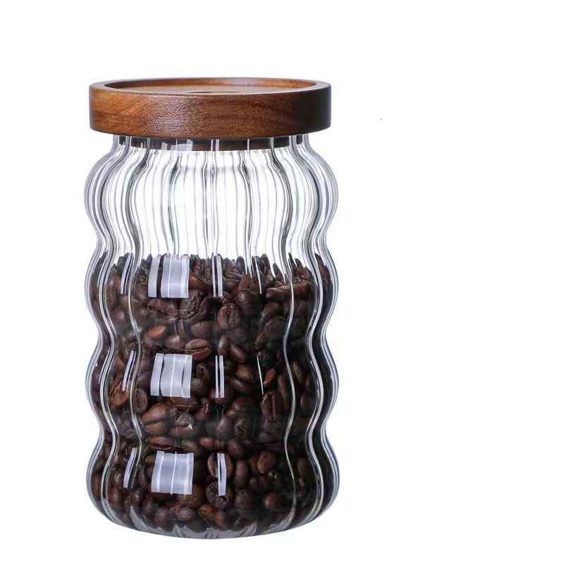 Clear glass jar with wavy design and wooden lid filled with coffee beans on a white background