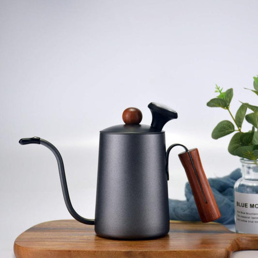 Black coffee kettle on a wooden surface with a plant and bottle in the background
