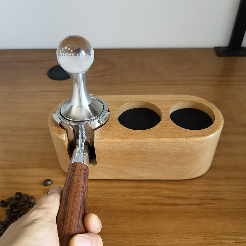A solid beechwood espresso tamping station with three circular slots and a portafilter holder. The station is designed to organize and hold coffee tools like a tamper, distributor, and a portafilter, preventing scratches on the countertop. Shop- now!
