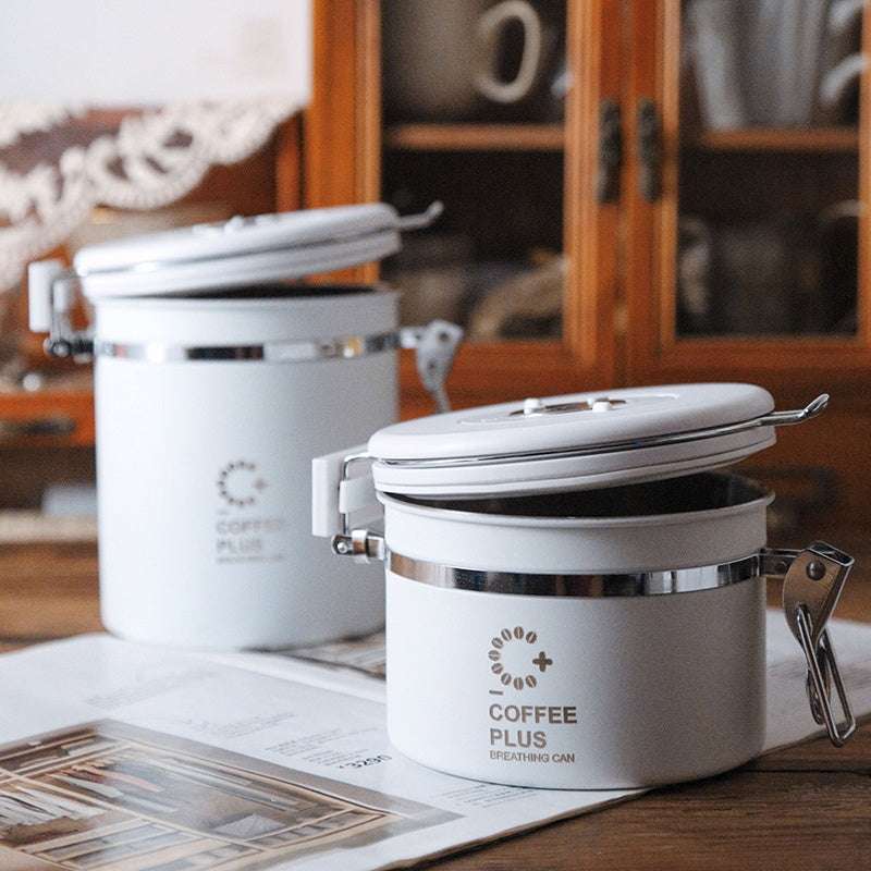  white Coffee Plus Breathing Canister, open to show dark roasted coffee beans inside. A one-way valve on the lid helps keep beans fresh.